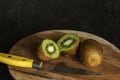 Ripe whole kiwi fruits and two half kiwi fruits on chopping board with knife with black wooden surface. Selective focus Royalty Free Stock Photo
