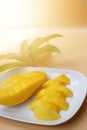 Ripe yellow mango, peeled and cut into pieces on a white plate, soft background, warm light.