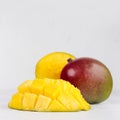 Ripe yellow mango whole with red and green side and pulpy sliced half closeup on soft white wood board, square.