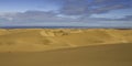 Rippled sand dunes of the Namib desert with a few clouds in the blue sky.