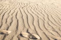 Rippled small sand on sea coast. Dunes on beach formed by wind and water. Footprints from shoes on sand