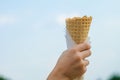 Rised up a waffle cone in the hand of a child on the sky background