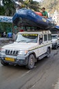 Car carrying a whitewater rafting boat drives through the street, with a man riding on top Royalty Free Stock Photo