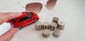 Driving small red fiat 500 abarth toy on white table near sunglasses and pile of Israeli shekel coins