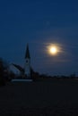 Rising full moon next to a catholic church