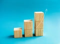 Rising up curved thin arrow draw on wooden cube blocks bar graph chart steps on blue background, minimal style.