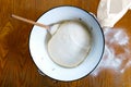 Rising yeast dough with wooden spoon in white enamel metal bowl Royalty Free Stock Photo