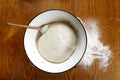 Rising yeast dough with wooden spoon in white enamel metal bowl