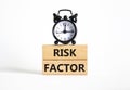Risk Factor symbol. Wooden blocks with words Risk Factor Beautiful white background with alarm clock. Business and Risk Factor Royalty Free Stock Photo
