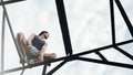 Risky man balancing and sitting on high metal construction Royalty Free Stock Photo