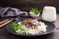 Risotto with mushrooms on a black plate. Boiled white rice with champignons in cream sauce. Dark wooden background. Copy