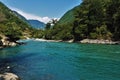 A river of aquamarine color flows between the slopes of the mountains covered with forest