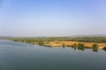 River bank with green forest and palm trees under a clear blue sky, view from the water Royalty Free Stock Photo