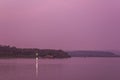 River bank with a house in a green forest under a purple sunset sky in the evening, view from the water Royalty Free Stock Photo