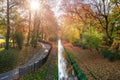 River and bicycle path in the city park in autumn. Sun rays shining through the branches of trees. Royalty Free Stock Photo