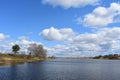 River, birch, pine. On the high banks are village houses, trees and green grass. There are white clouds in the blue sky. Wind