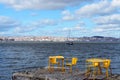 River boat on the Lisbon background. Yellow chairs and tables in riverside cafe in Almada. Portugal.
