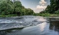 A river in the countryside with turbulent stream rapids. Summertime, long exposure shot of rural scene. The river banks overgrown Royalty Free Stock Photo