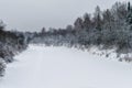 River covered with ice and snow from the forested shores and cloudy sky.