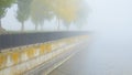 River embankment with a fence and autumn trees in fog. Royalty Free Stock Photo