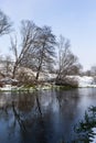 The river flows through the forest. In late fall in the forest the trees stand leafless and reflected in the water of the river