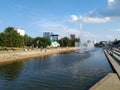 View of the waterfront. River with fountains. On the banks are the steps of the asphalt road. People walk, there are buildings and