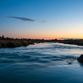 River with gentle ripples flows under a clear evening sky transitioning from blue to Royalty Free Stock Photo