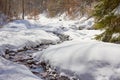 River meandering through snow on a sunny day, during a hiking trip in Bucegi mountains, Romania, in Winter