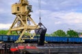 River port crane with clamshell or griper loading coal to river drag boats or barges moored by pier on cloudy day Royalty Free Stock Photo