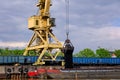 River port crane with clamshell or griper loading coal to river drag boats or barges moored by pier on cloudy day Royalty Free Stock Photo