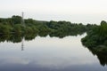 River with reflected clouds, forest on the banks of the river and power transmission tower.