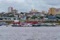 River view of a ferry refueling at a floating fuel station at the port of Manaus, with city skyscrapers visible in the background