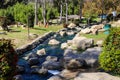 A river with water rushing over the rocks in the park surrounded by autumn trees and lush green grass with blue sky Royalty Free Stock Photo