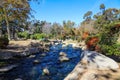 A river with water rushing over the rocks in the park surrounded by autumn trees and lush green grass with blue sky Royalty Free Stock Photo