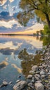 Riverside at sunset, clouds reflected in the still water, stones in the foreground, and trees framing the sky Royalty Free Stock Photo
