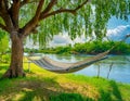 A riverside view with a hammock swaying gently in the breeze under shady trees