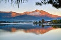 The riverside village and mountains reflect the water in the misty morning at Lake Wolfgang