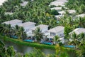 Riverside white painted tropical villas with swimming pool, lounge chairs surrounding lush green coconut palm trees, row upscale