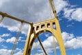 Riveted metal self anchored suspension bridge painted yellow against a bright blue sky with white puffy clouds Royalty Free Stock Photo