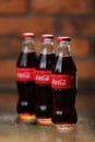 RIVNE, UKRAINE JUNE 26 2020: three Classic glass bottles Of Coca-Cola on brick wall background. cans of coca-cola