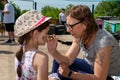 RIVNE, UKRAINE - JUNE 19, 2022. Woman painting on girl`s face outdoor. Girl getting her face painted by face painting artist Royalty Free Stock Photo