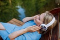 Rlaxed woman wearing headphones listening to music lying on a pier by natureal lake in summer Royalty Free Stock Photo