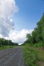 The road against the background of blue sky with white clouds on a bright sunny summer day. Part of birch trees with green foliage