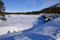 Road Bridge over snowed over frozen river, Aust-Agder, Norway. Trees behind. Blue skies.