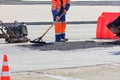 The road builder evenly distributes part of the asphalt with a wooden level on a part of the road fenced with an orange cone and a Royalty Free Stock Photo