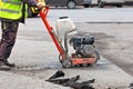 A road builder in reflective overalls uses a portable asphalt cutter to cut asphalt to repair a section of the roadway