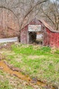 Road and creek next to old faded red barn in midwest with dead forest Royalty Free Stock Photo