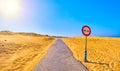 A road crossing an arid dune terrain with a No overtaking sign