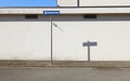 Road directional arrow sign on sidewalk. White plaster facade on behind and urban road in front.