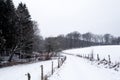 Road between fields and forests covered with snow in a winter landscape.